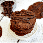 Stack of triple chocolate caramel cookies on a small white stand with a jar of chocolate chips behind it