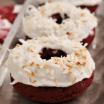 Three baked toasted coconut red velvet donuts in a row on a silver serving tray