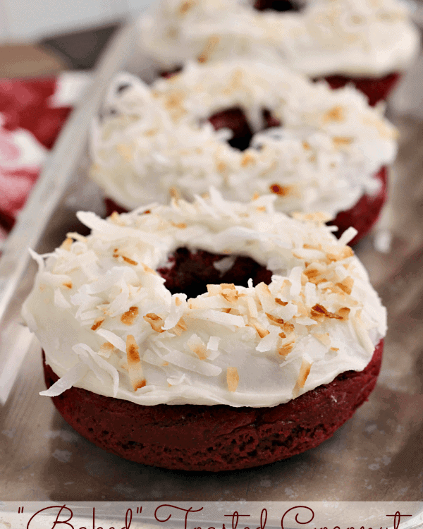 Three baked toasted coconut red velvet donuts in a row on a silver serving tray