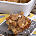 Piece of overnight banana caramel french toast on a plate with a fork in front of a white baking dish containing the rest of the french toast