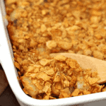 White baking dish of mom's cottage potatoes with a wooden spoon scooping potatoes out