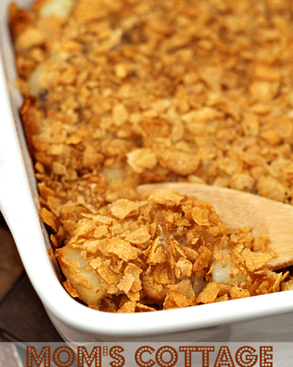 White baking dish of mom's cottage potatoes with a wooden spoon scooping potatoes out