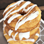 Three drizzled snickerdoodle donuts stacked on a brown and white plate