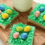 Three Easter egg hunt sugar cookie bars on a wood board with a glass of milk