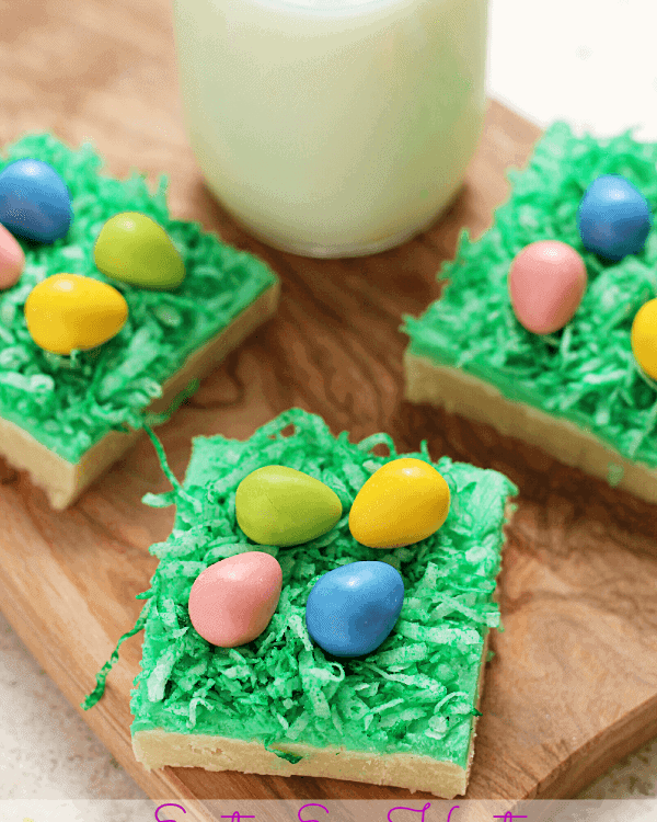 Three Easter egg hunt sugar cookie bars on a wood board with a glass of milk
