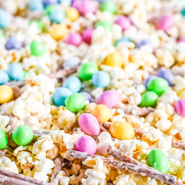 Snack mix spread out on wax paper with popcorn pretzels m&ms and peanuts with candy melts coating