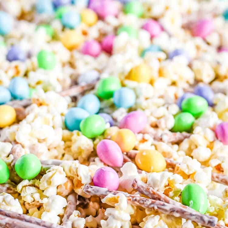 Snack mix spread out on wax paper with popcorn pretzels m&ms and peanuts with candy melts coating