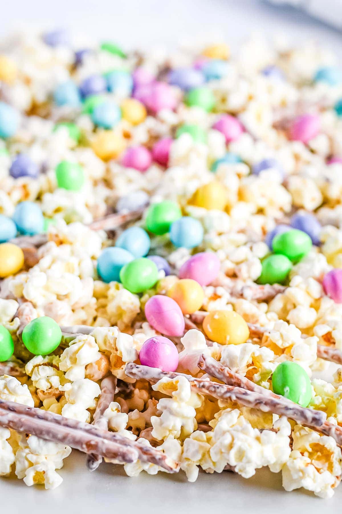 Snack mix spread out on wax paper with popcorn pretzels m&ms and peanuts with candy melts coating