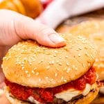 Hand holding burger with marinara sauce and mozzarella on it