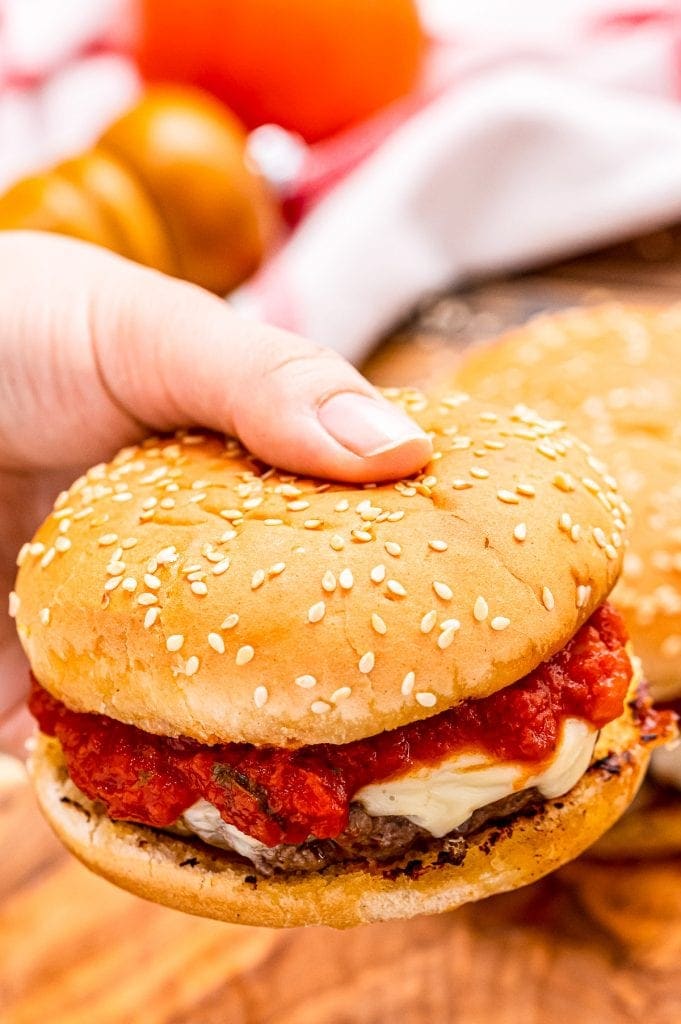 Hand holding burger with marinara sauce and mozzarella on it