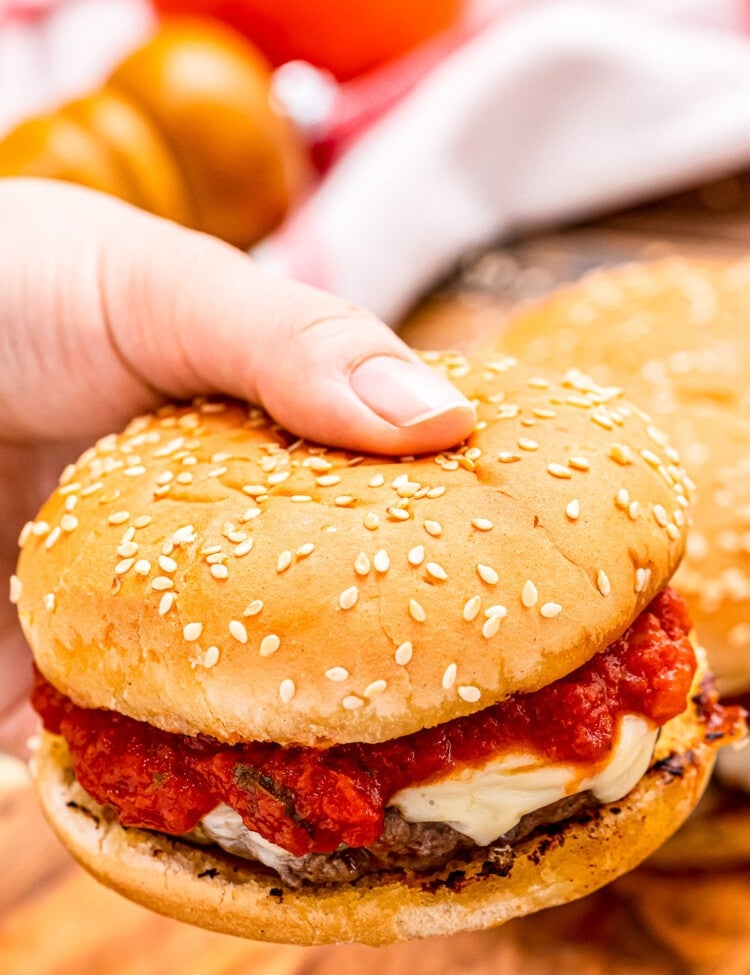 Hand holding burger with marinara sauce and mozzarella on it