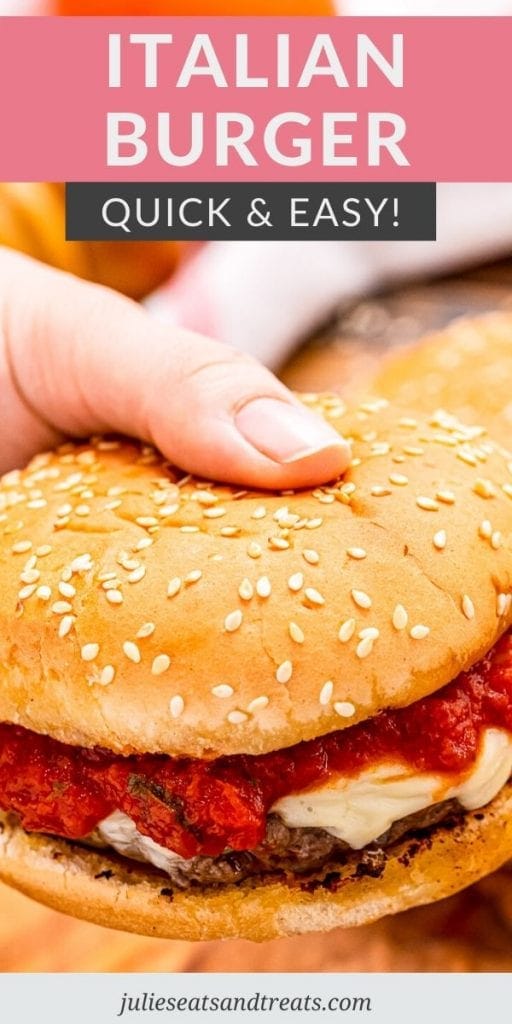 Hand holding an Italian burger topped with cheese and marinara sauce