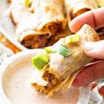 Hand holding a pulled pork taquito and dipping it in sauce