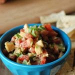 Blue bowl of peach and tomato salsa on a table with tortilla chips