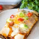 Pork enchilada on a white plate topped with tomato and avocado