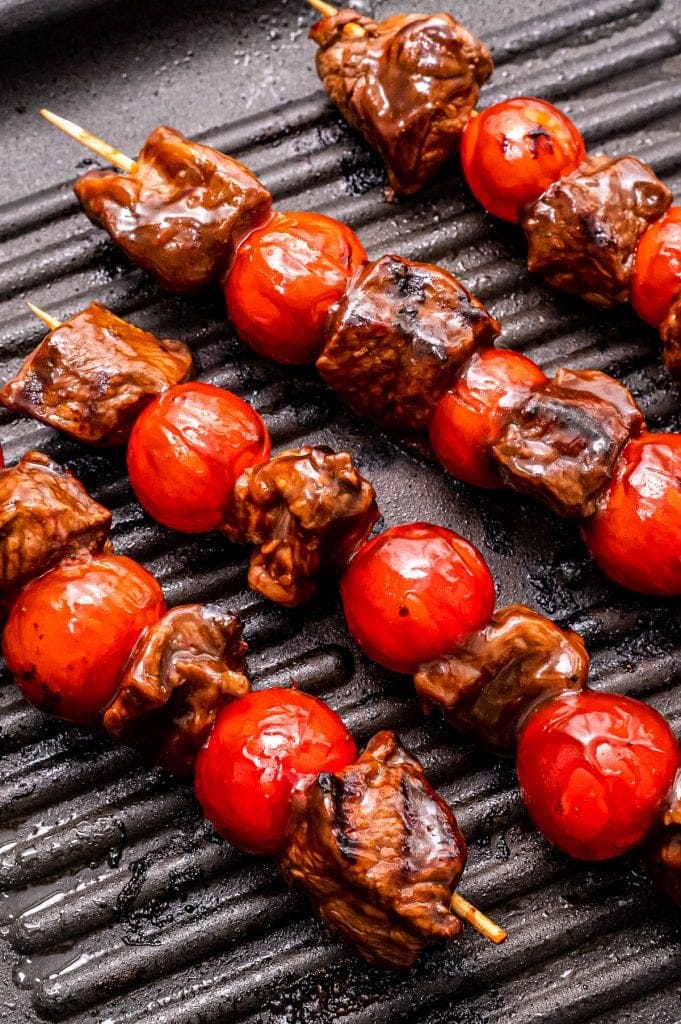 Grill pan with steak kabobs in it and grill marks on steak and cherry tomatoes