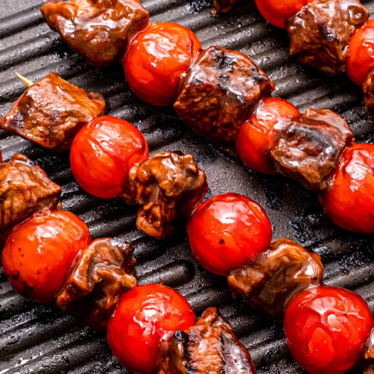 Grill pan with steak kebabs in it and grill marks on steak and cherry tomatoes