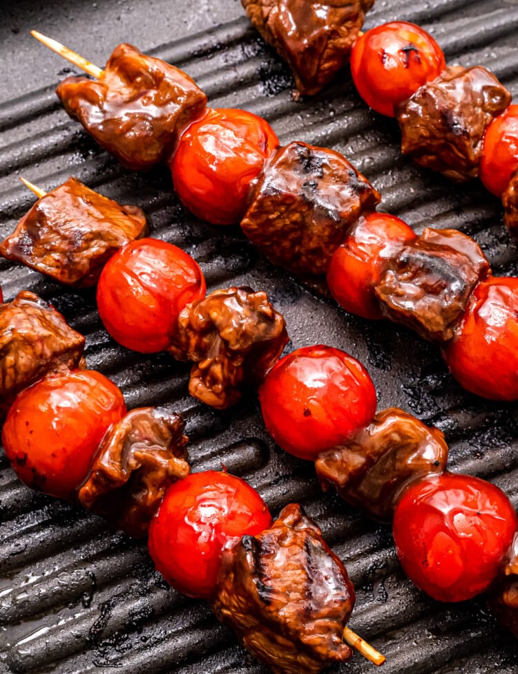 Grill pan with steak kebabs in it and grill marks on steak and cherry tomatoes