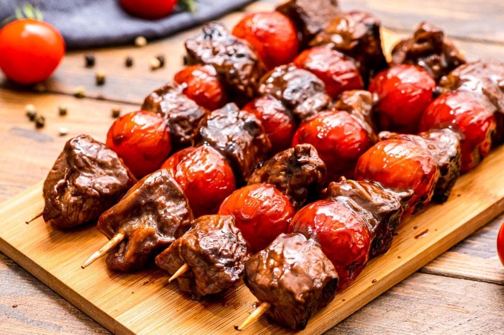 Wood cutting board with steak and cherry tomato kabobs on it