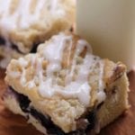 Two pieces of blueberry cream cheese coffee cake on a wood board with a glass jar of milk