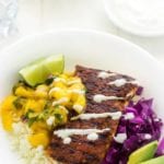 Fish taco bowl containing fish, avocado, limes, cabbage, and rice