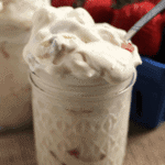 Two glass jars of strawberry banana pudding fluff next to a blue bowl of strawberries