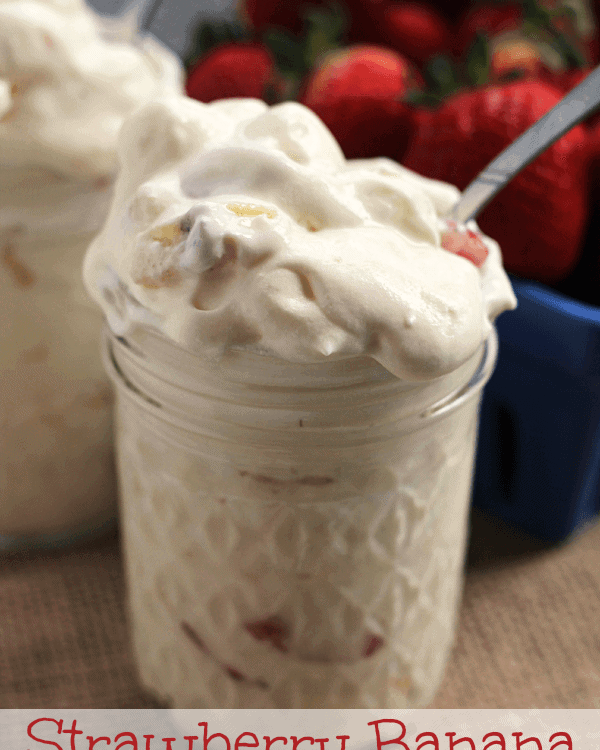 Two glass jars of strawberry banana pudding fluff next to a blue bowl of strawberries