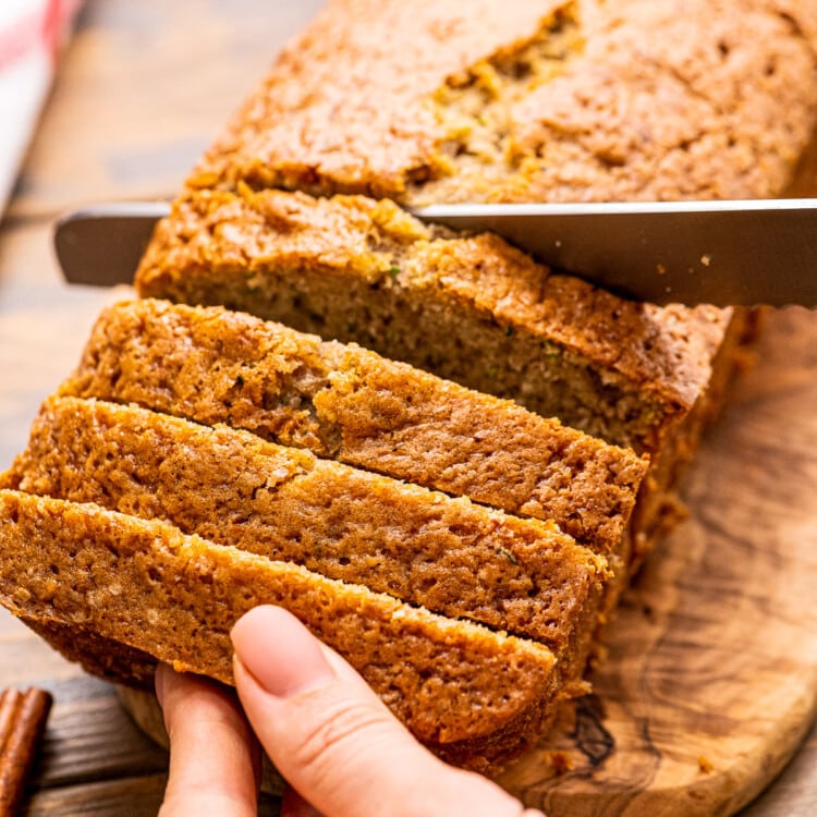 Hand holding a loaf of Banana Zucchini Bread while a knife slices it.