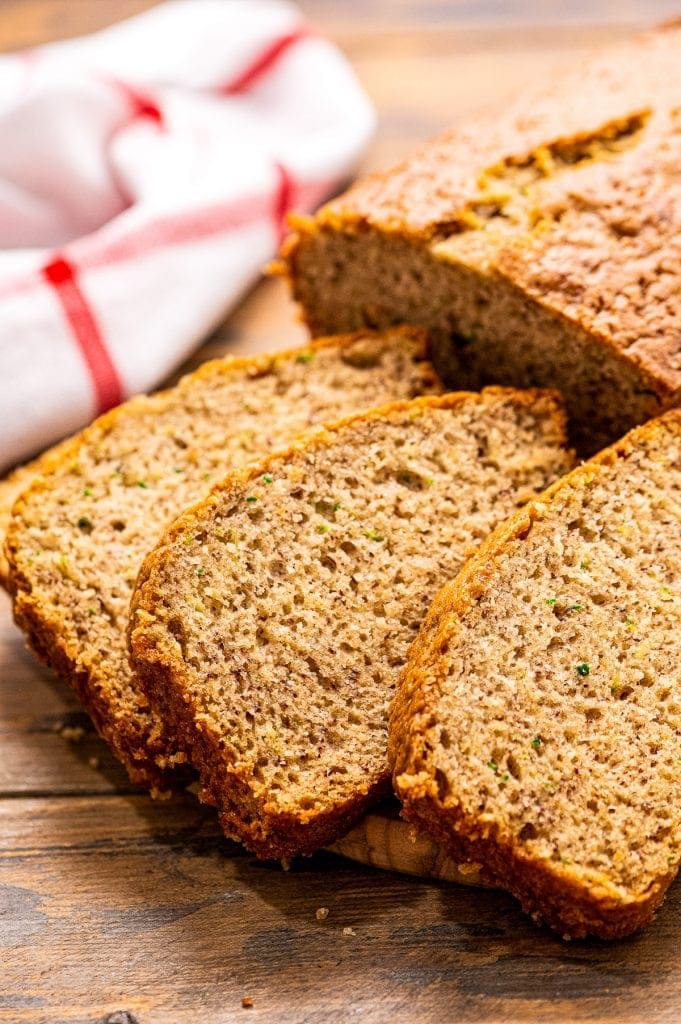 Three slices of Banana Zucchini Bread on wooden background with red and white striped napkin behind it.