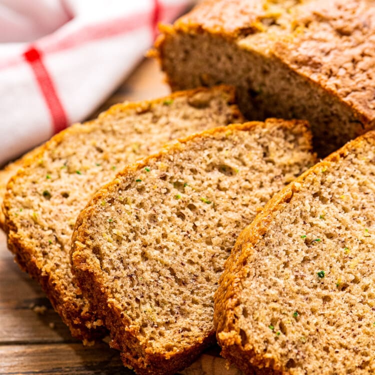 Three slices of Banana Zucchini Bread on wooden background with red and white striped napkin behind it.