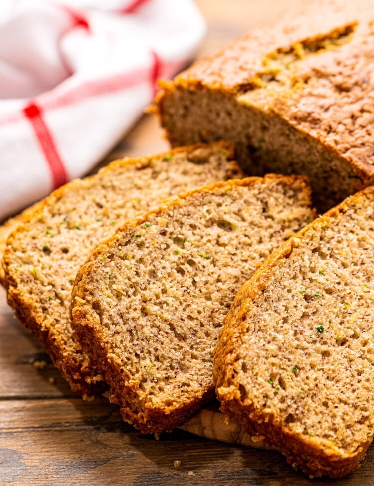 Three slices of Banana Zucchini Bread on wooden background with red and white striped napkin behind it.