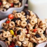 Two bowls of cheerios snack mix and a glass of milk on a table