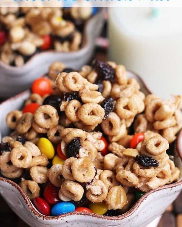 Two bowls of cheerios snack mix and a glass of milk on a table