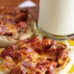 Two Cheesy ham and bacon English muffins on a yellow napkin with a glass of milk