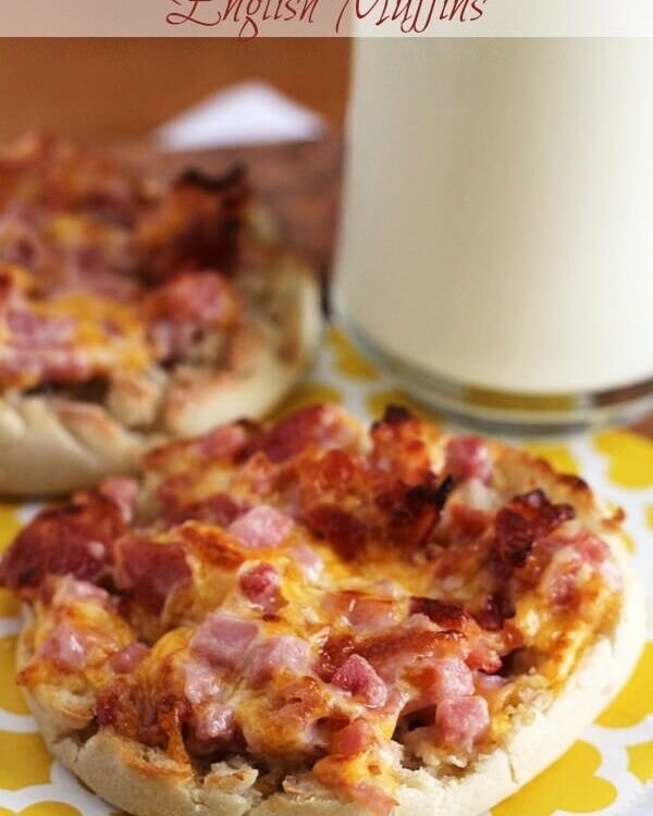 Two Cheesy ham and bacon English muffins on a yellow napkin with a glass of milk
