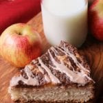 A slice of Cinnamon apple cream cheese coffee cake on a wood board with two apples and a glass of milk