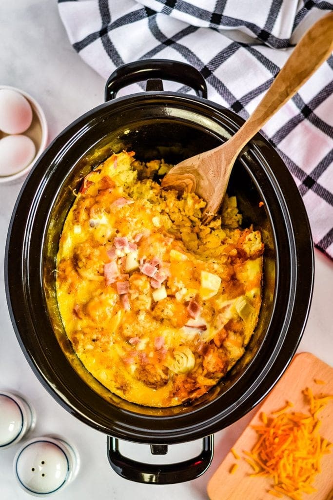 Overhead image of crock pot with tater tot egg bake with spoon scooping