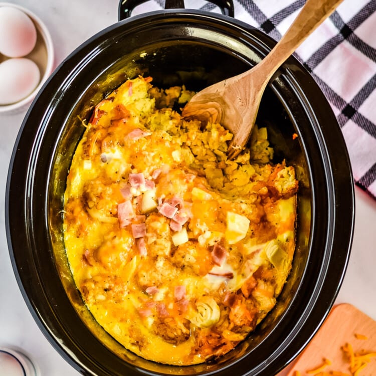 Overhead image of crock pot with tater tot egg bake with spoon scooping