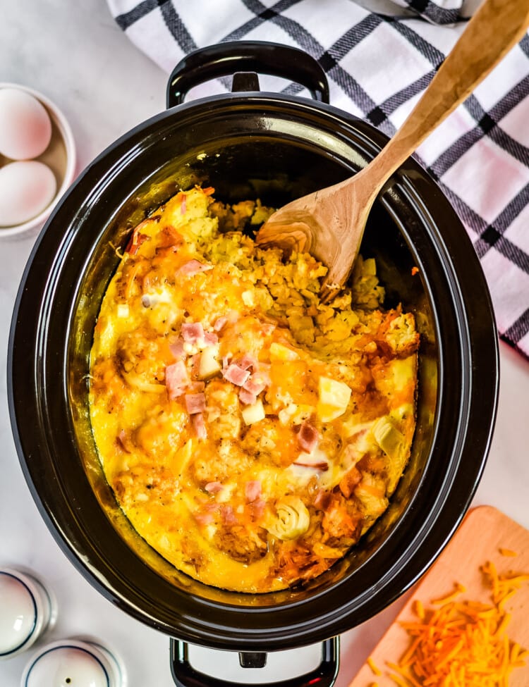 Overhead image of crock pot with tater tot egg bake with spoon scooping
