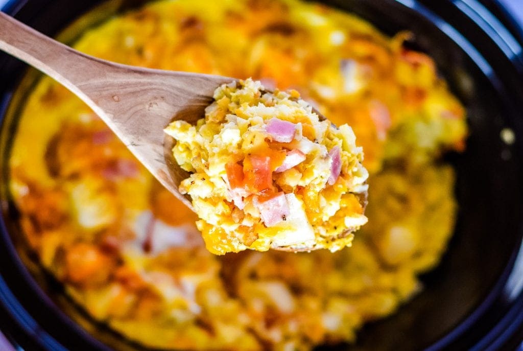 Wooden Spoon being held over crock pot with egg bake on it