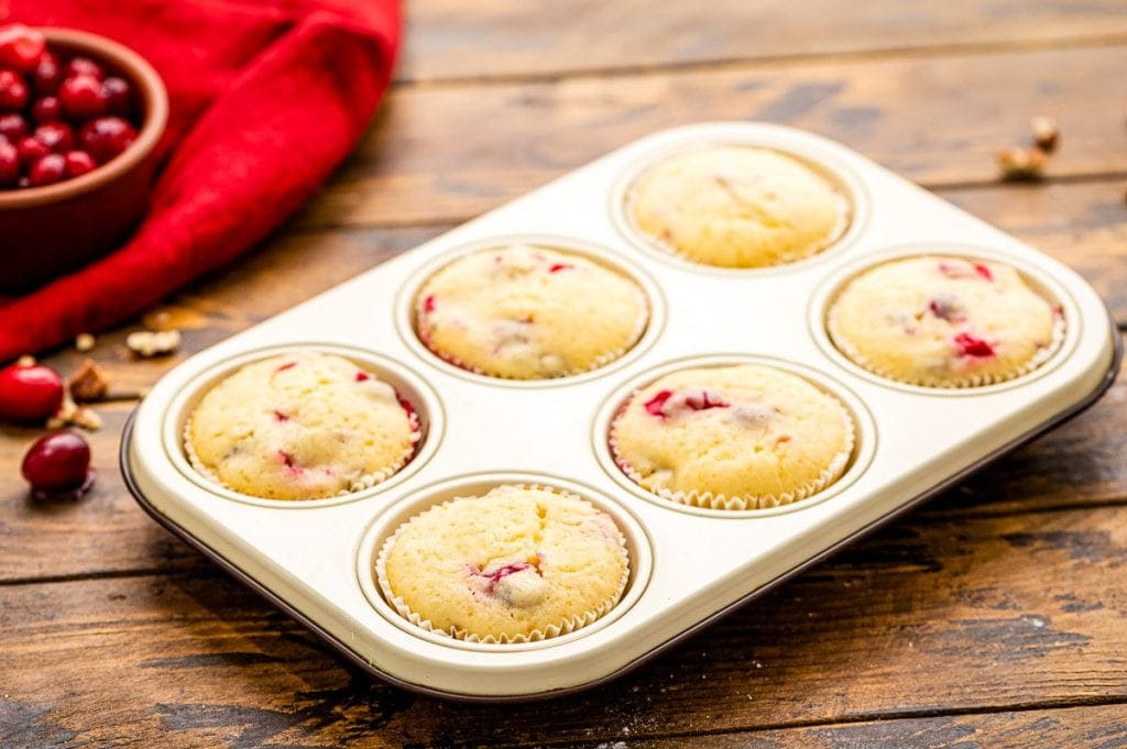 Muffin tin with 6 cranberry muffins that are baked.