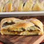 Slice of pumpkin cream cheese crescent braid on a wood board in front of the rest of the braid on a white plate