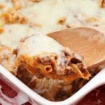 White baking dish of mom's pizza casserole with a wood spoon scooping pasta out