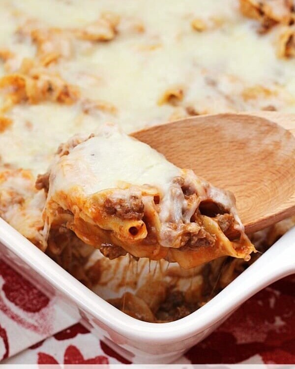 White baking dish of mom's pizza casserole with a wood spoon scooping pasta out