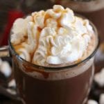 Two clear glass mugs of crock pot caramel hot chocolate topped with whipped cream and caramel sauce