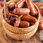 Two orange bowls stacked on a wood board with the top full of crock pot sweet bacon smokies