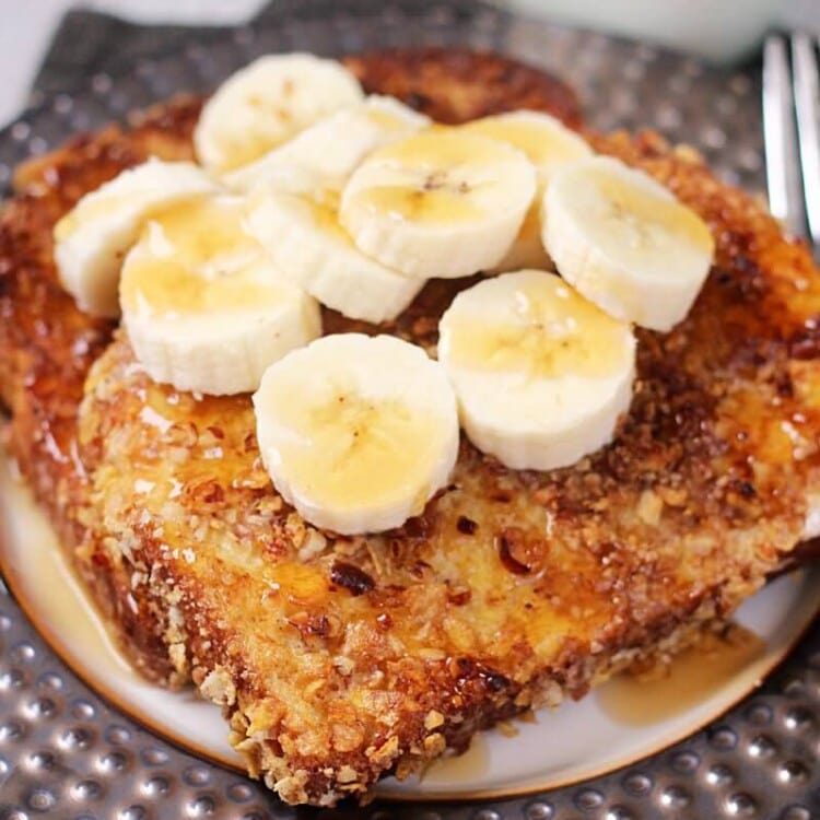 Two slices of crunchy pecan banana french toast topped with banana slices and syrup on a round plate