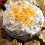 Brown bowl of kickin' ranch corn dip topped with shredded cheese on a wood board with corn chips