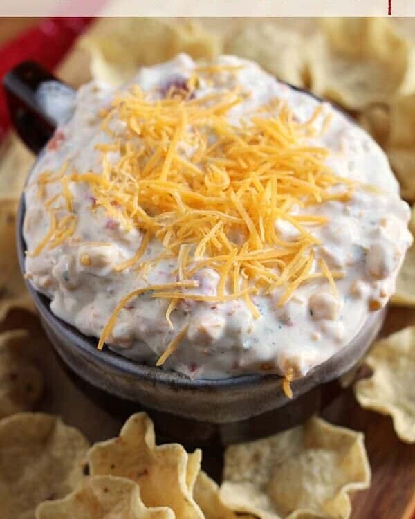 Brown bowl of kickin' ranch corn dip topped with shredded cheese on a wood board with corn chips