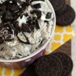 Purple bowl of cookies and cream dip on a yellow napkin next to stacks of Oreo cookies